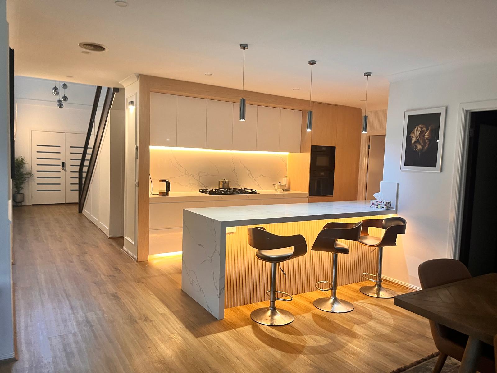 Renovated kitchen with warm timber cabinetry, stone island and softly lit finishes, opening to the adjoining living areas
