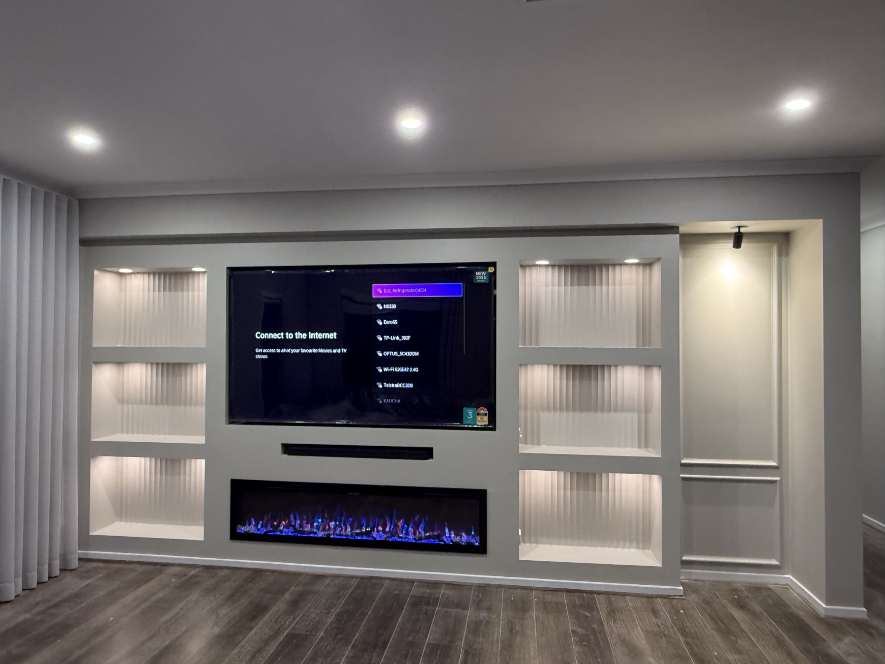 Finished media wall with a television, softly lit display niches, concealed joinery and a linear fireplace